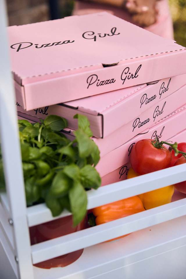 Stacked pink Pizza Girl boxes with fresh basil and tomatoes