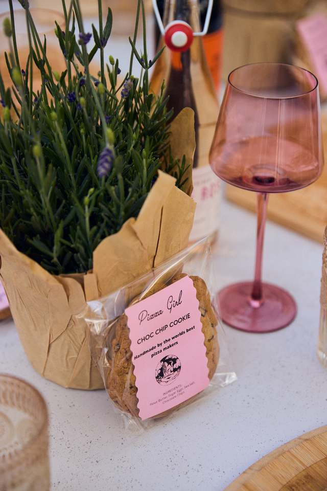 Pizza Girl cookie favor beside a rose-tinted wine glass on a styled table